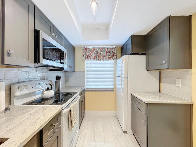 kitchen featuring a raised ceiling, light stone counters, stainless steel appliances, and tasteful backsplash