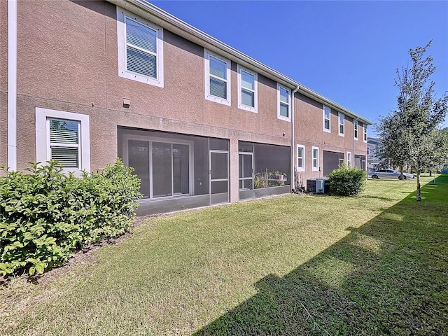 rear view of house with central AC unit, a sunroom, and a lawn