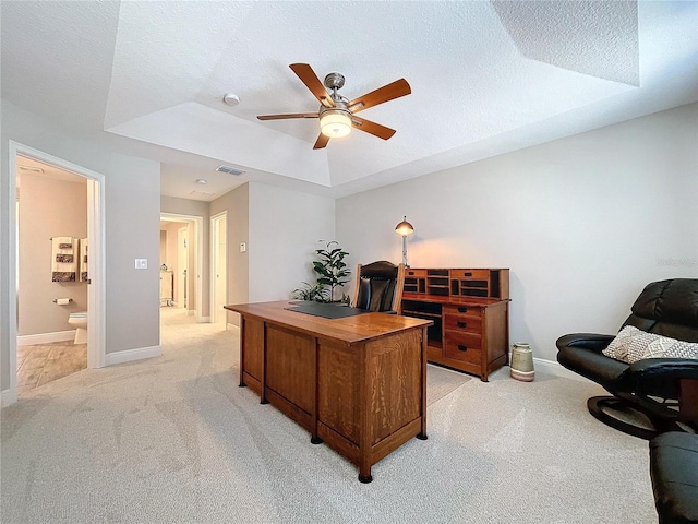 carpeted home office featuring a textured ceiling, a tray ceiling, and ceiling fan