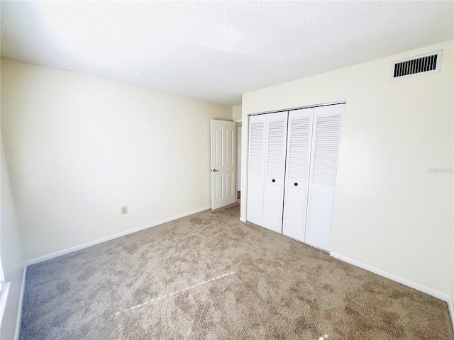 unfurnished bedroom with light colored carpet, a closet, and a textured ceiling