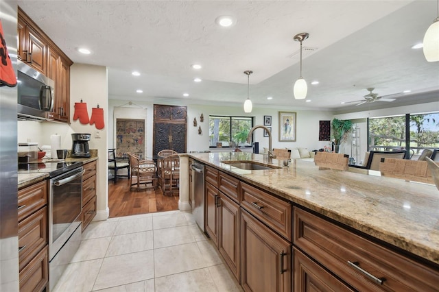 kitchen with light stone countertops, appliances with stainless steel finishes, sink, hanging light fixtures, and light tile patterned floors