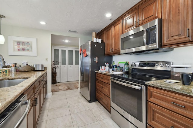 kitchen with light stone countertops, sink, a textured ceiling, hanging light fixtures, and stainless steel appliances