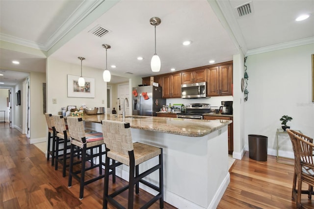 kitchen featuring appliances with stainless steel finishes, a breakfast bar, ornamental molding, dark wood-type flooring, and pendant lighting