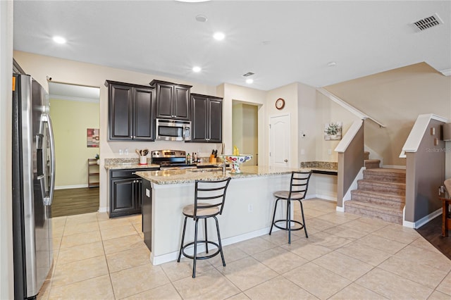 kitchen with light stone countertops, appliances with stainless steel finishes, a center island with sink, and a kitchen breakfast bar