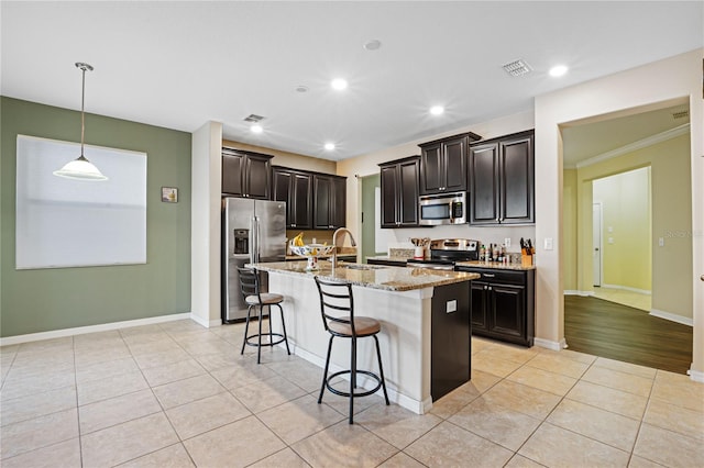 kitchen featuring crown molding, appliances with stainless steel finishes, an island with sink, light stone counters, and a breakfast bar