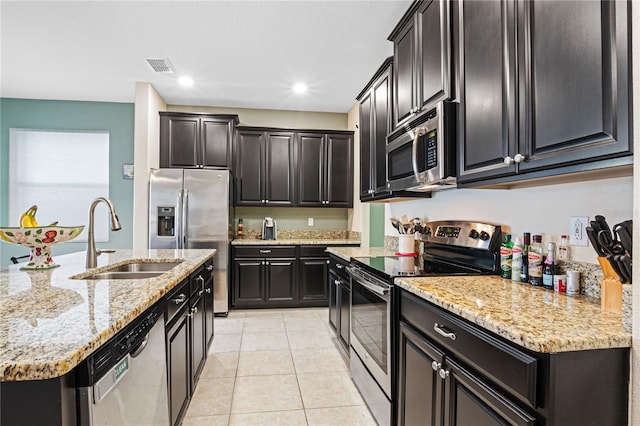 kitchen featuring a center island with sink, appliances with stainless steel finishes, light stone countertops, light tile patterned flooring, and sink