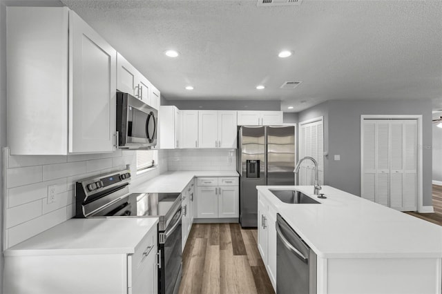 kitchen with white cabinets, a center island with sink, dark hardwood / wood-style floors, sink, and stainless steel appliances