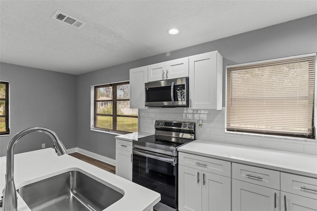 kitchen with decorative backsplash, sink, white cabinets, appliances with stainless steel finishes, and a textured ceiling