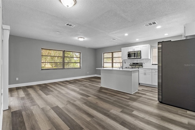 kitchen featuring a kitchen island with sink, appliances with stainless steel finishes, dark wood-type flooring, and white cabinets