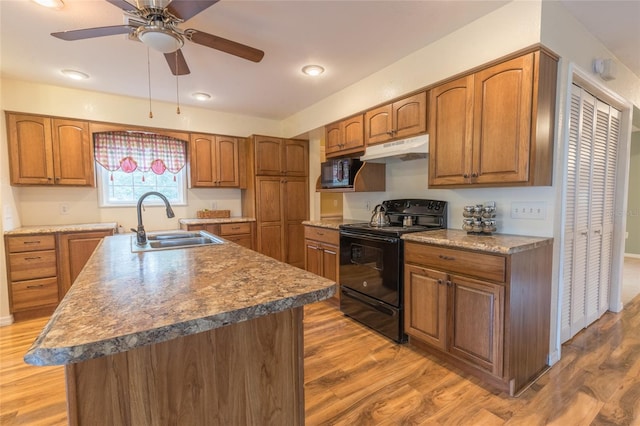 kitchen with black appliances, sink, ceiling fan, hardwood / wood-style flooring, and a kitchen island with sink