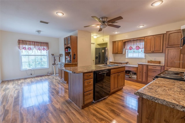 kitchen with sink, black appliances, a kitchen island with sink, and hardwood / wood-style flooring