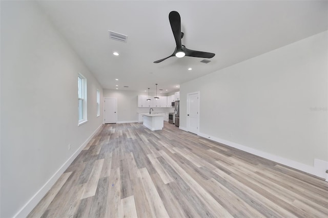 unfurnished living room with sink, ceiling fan, and light wood-type flooring