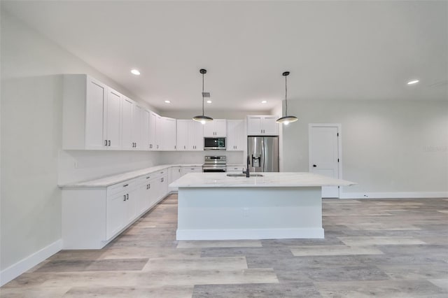 kitchen featuring stainless steel appliances, white cabinetry, decorative light fixtures, and an island with sink