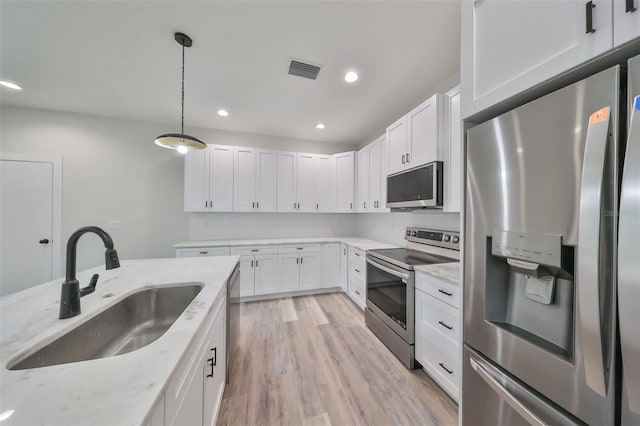 kitchen featuring stainless steel appliances, sink, white cabinetry, hanging light fixtures, and light stone countertops