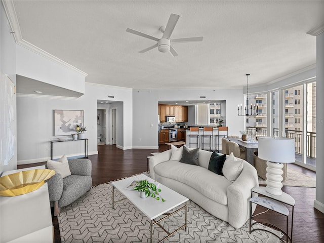 living area with a textured ceiling, ceiling fan with notable chandelier, dark wood-type flooring, baseboards, and crown molding