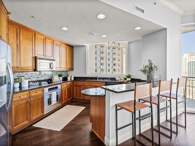 kitchen featuring brown cabinets, visible vents, stainless steel appliances, and dark stone countertops