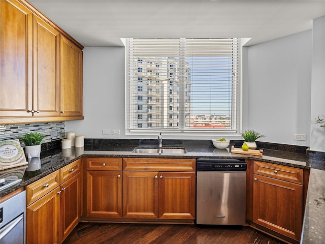 kitchen with stainless steel appliances, a sink, brown cabinets, tasteful backsplash, and dark stone countertops