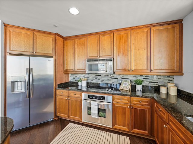 kitchen with appliances with stainless steel finishes, dark hardwood / wood-style floors, backsplash, and dark stone counters