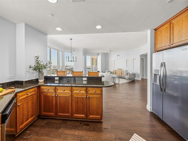 kitchen featuring kitchen peninsula, stainless steel appliances, dark stone counters, pendant lighting, and dark hardwood / wood-style floors