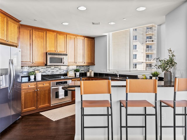 kitchen featuring brown cabinets, a kitchen bar, stainless steel appliances, and dark stone countertops