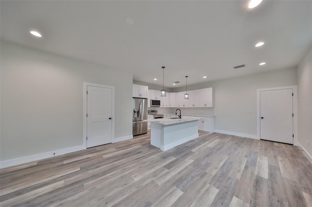 kitchen featuring decorative light fixtures, stainless steel appliances, an island with sink, white cabinetry, and sink