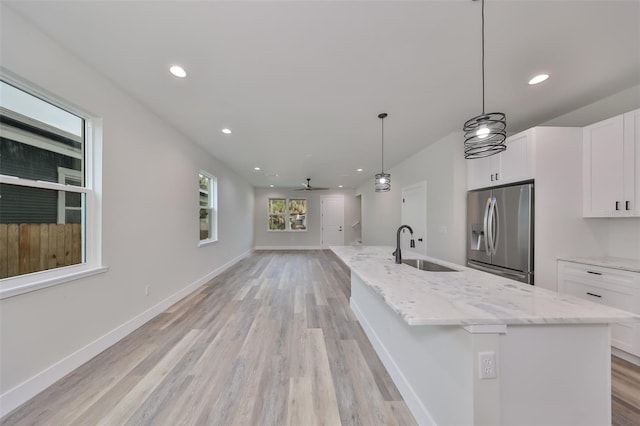 kitchen with a center island with sink, stainless steel refrigerator with ice dispenser, white cabinetry, ceiling fan, and sink