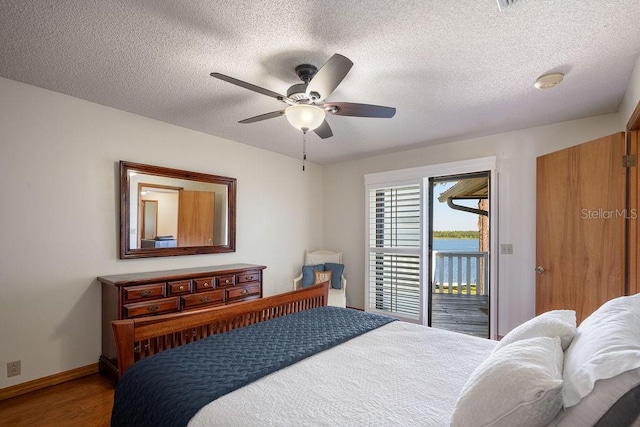 bedroom with hardwood / wood-style floors, ceiling fan, access to outside, a textured ceiling, and a water view