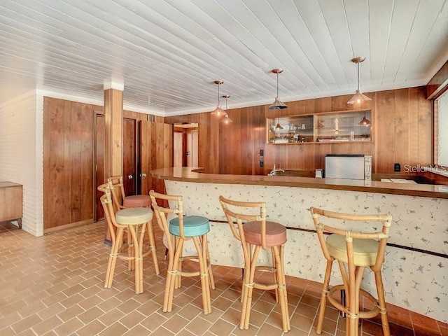 bar with decorative light fixtures, fridge, ornamental molding, and wooden walls