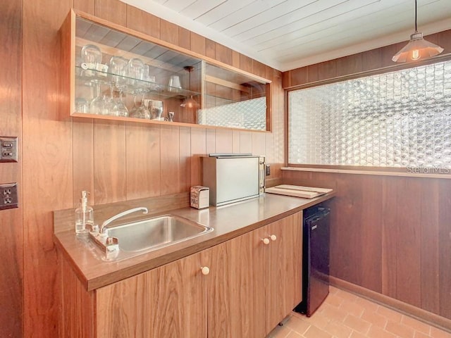 kitchen featuring decorative light fixtures, black dishwasher, wooden walls, sink, and light tile patterned floors