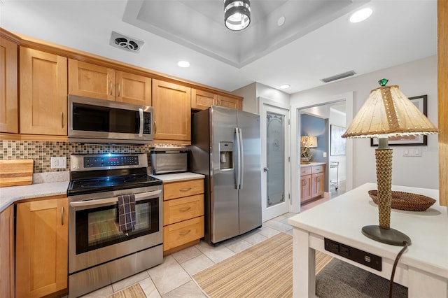 kitchen with a tray ceiling, stainless steel appliances, backsplash, and light tile patterned floors