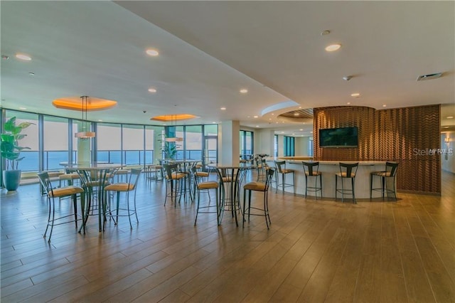 dining area with expansive windows, hardwood / wood-style floors, a healthy amount of sunlight, and a water view