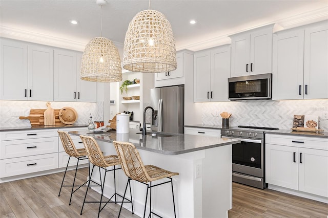 kitchen featuring a kitchen island with sink, light hardwood / wood-style flooring, hanging light fixtures, stainless steel appliances, and white cabinetry