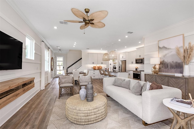 living room with ornamental molding, light wood-type flooring, and ceiling fan