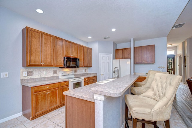 kitchen with a breakfast bar area, a center island with sink, sink, light tile patterned floors, and white appliances