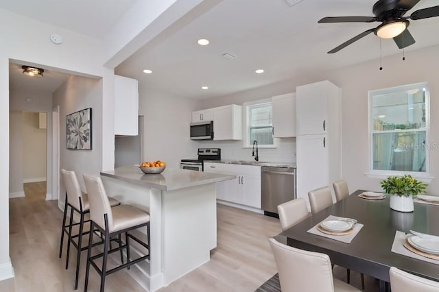 kitchen featuring white cabinets, appliances with stainless steel finishes, a breakfast bar area, light countertops, and a sink