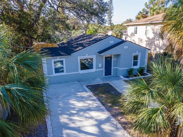 view of front of house featuring a patio, a shingled roof, fence, and stucco siding