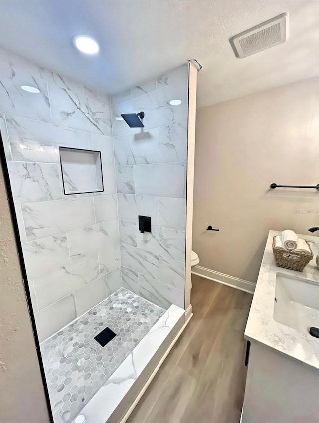 bathroom featuring double vanity, visible vents, toilet, wood finished floors, and a tile shower