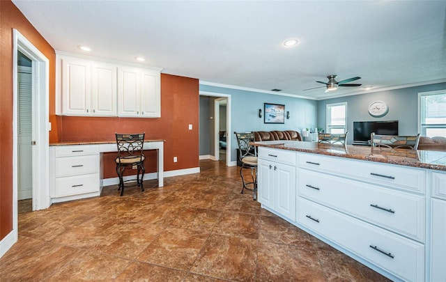 kitchen featuring built in desk, ornamental molding, white cabinets, and ceiling fan