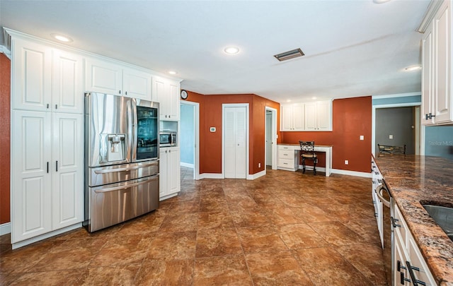 kitchen featuring appliances with stainless steel finishes, white cabinets, dark stone countertops, and built in desk