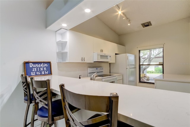 kitchen featuring kitchen peninsula, vaulted ceiling, a kitchen bar, white cabinetry, and white appliances