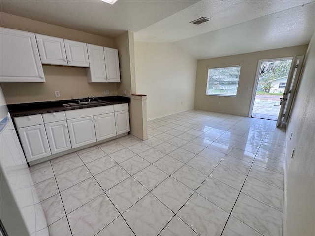 kitchen featuring light tile patterned floors, a textured ceiling, white cabinetry, vaulted ceiling, and sink