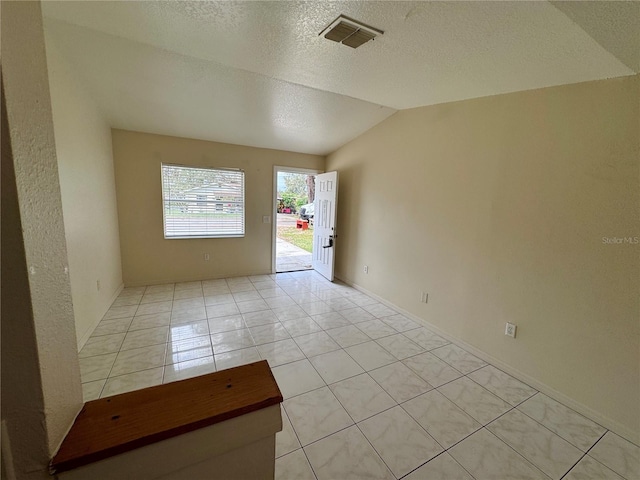 tiled empty room featuring a textured ceiling and lofted ceiling