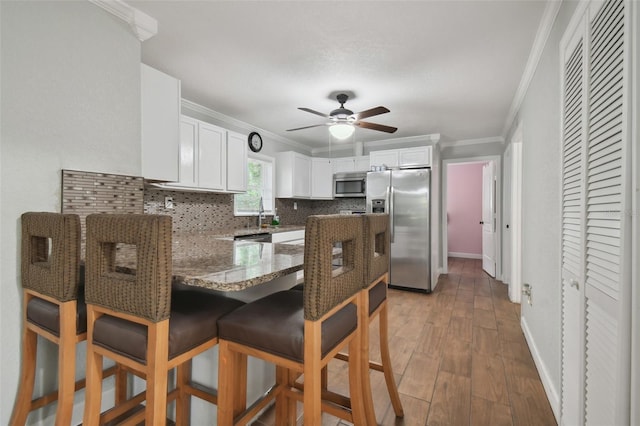 kitchen with white cabinetry, crown molding, appliances with stainless steel finishes, kitchen peninsula, and decorative backsplash