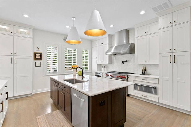 kitchen featuring wall chimney range hood, white cabinets, sink, and appliances with stainless steel finishes