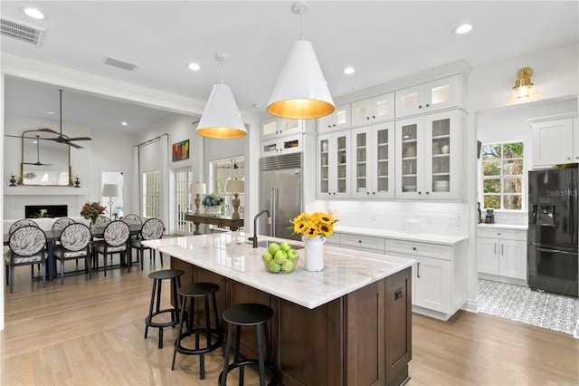 kitchen featuring stainless steel built in fridge, white cabinetry, a kitchen island with sink, and black fridge with ice dispenser