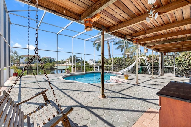 view of pool with a water view, a water slide, glass enclosure, and a patio area