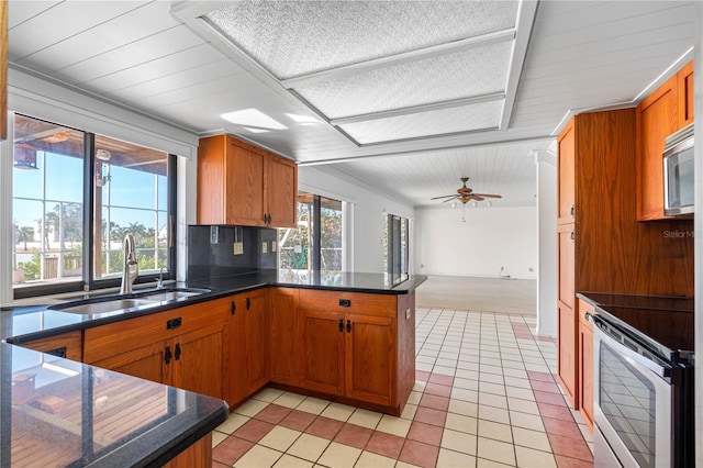 kitchen featuring brown cabinetry, dark countertops, appliances with stainless steel finishes, a peninsula, and a sink