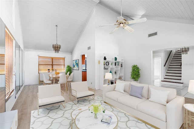 living area featuring light wood-type flooring, stairs, visible vents, and ceiling fan with notable chandelier