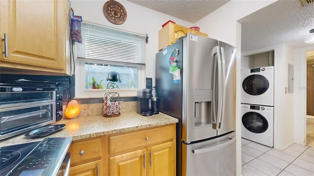 kitchen with light stone countertops, a textured ceiling, stainless steel fridge, stacked washing maching and dryer, and light tile patterned floors