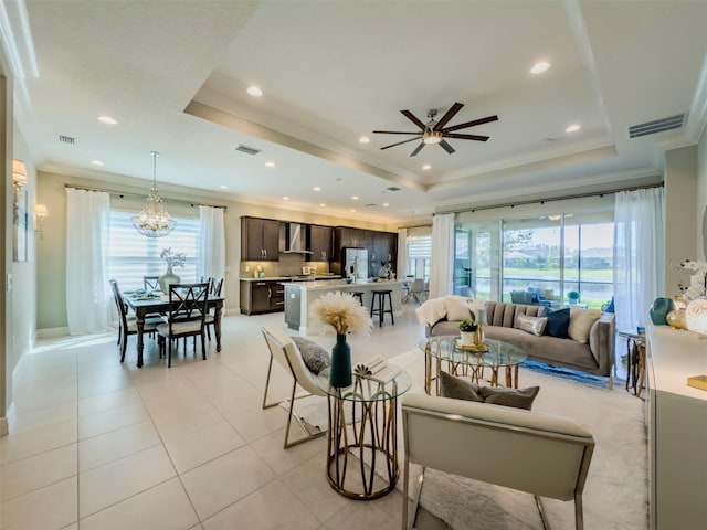 living room featuring ceiling fan with notable chandelier, ornamental molding, a tray ceiling, and light tile patterned floors